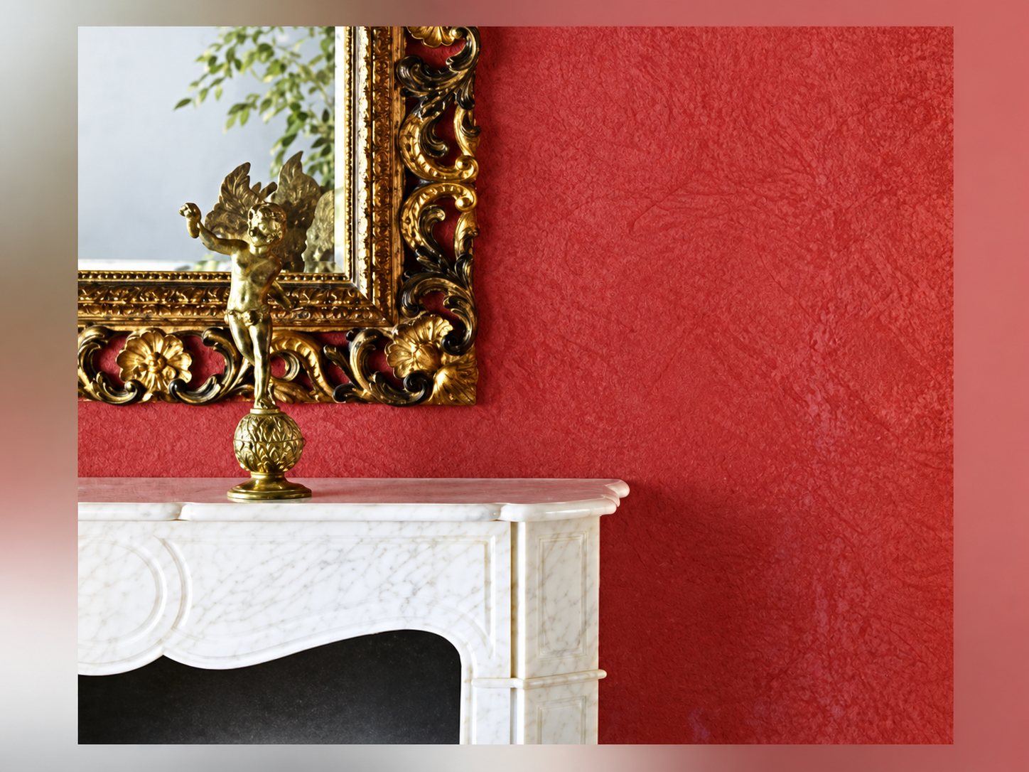 Un mur rouge à l'enduit décoratif patiné surmonte une cheminée en marbre blanc ornée d'une statuette dorée et d'un miroir à cadre doré sculpté.